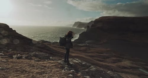Woman Hiker Stands on Cliff Above Wavy Ocean