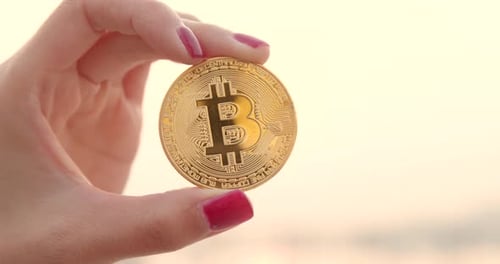 Woman Holds Gold Bitcoin in Fingers Close Up