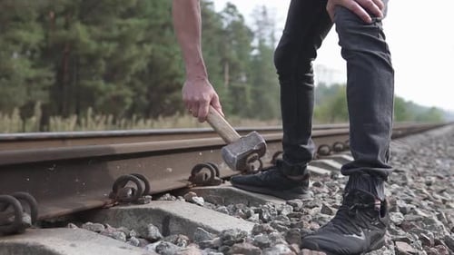 A Railway Man in a Helmet Repairs a Railway, Hammering the Spire with a Sledgehammer