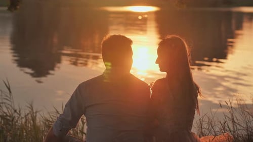 A Young Couple Sits on a Lake at Sunset.