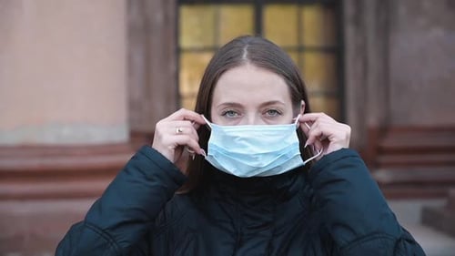 Woman Puts on Light Blue Surgical Mask Outdoors