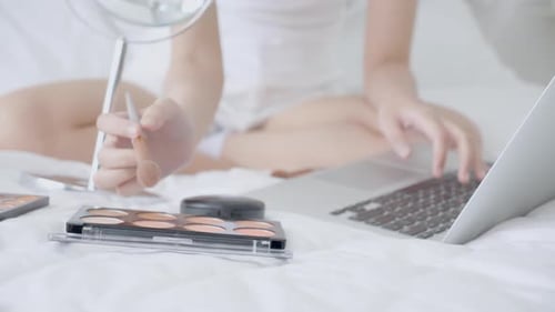 Manos de mujer con aprendizaje de maquillaje con pincel en la mejilla en computadora portátil con tutorial.