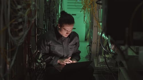 Adult working on laptop in dark server room