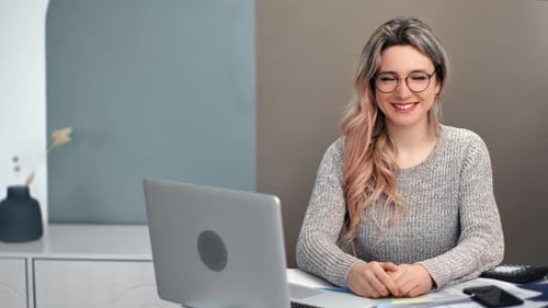 Smiling Woman Sits at Desk with Laptop