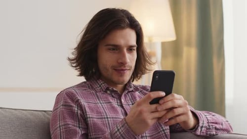 Close Up Portrait of Young Man Texting Online on Smartphone Sitting at Home Alone