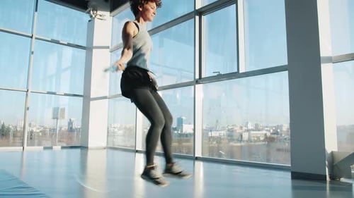 Young Woman in Sportswear Jumping with Skipping Rope Indoors in Modern Gym