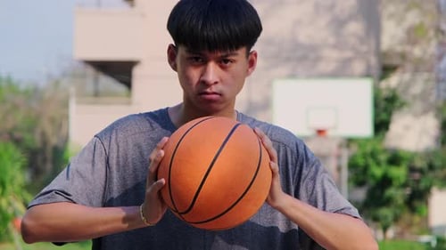Young Asian athlete holding basketball at outdoor court