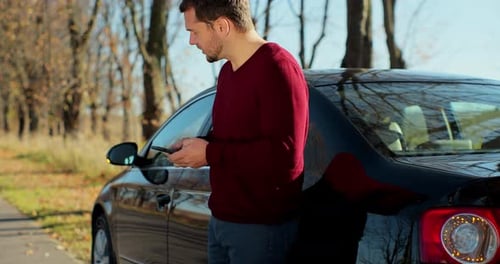 Distressed Man Looking at Cell Phone By Car