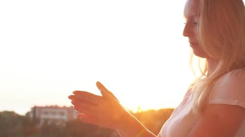 Woman Applying Skincare Cream on Hands in Sunlight