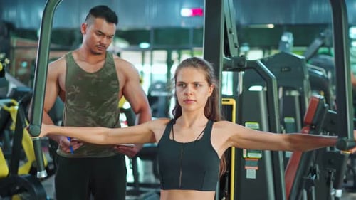 Asian Fitness trainer motivate young sportswoman or athlete exercise by lifting dumbbell in gym.