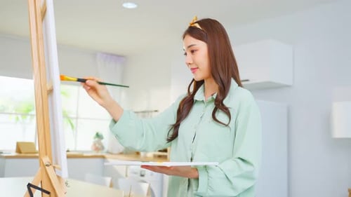 Asian young talented woman artist coloring on painting board in house.