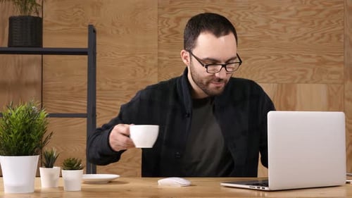 Young Bearded Man Drinking Coffee or Tea While Working on Laptop