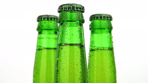Three green glass bottles of beer turning over white background