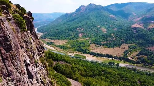 Fliegen am felsigen Berg mit Blick auf eine Schlucht, einen Fluss und weit entfernte Berge