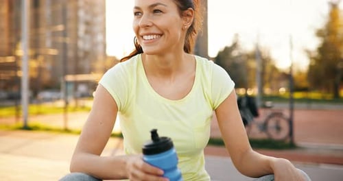 Smiling Woman Drinking Water After Workout in City