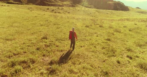 Flight Over Backpack Hiking Tourist Walking Across Green Mountain Field. Huge Rural Valley at Summer