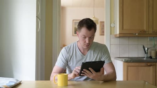 Young Adult Using Tablet Device at Kitchen Table
