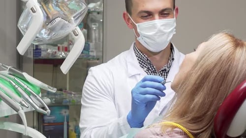 Männlicher Zahnarzt mit medizinischer Maske untersucht Zähne einer Patientin