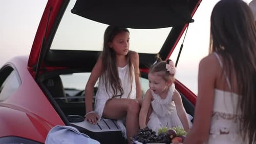 Two Girls Sitting in Car Trunk at Beach