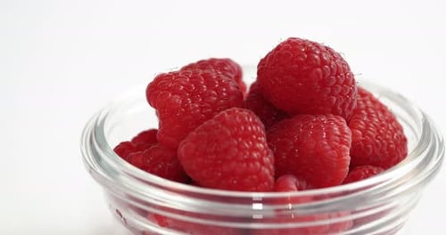Glass Dish Of Raspberries Moving Across White Background