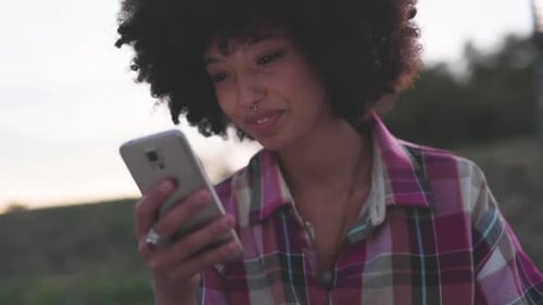 Smiling Young Adult Looks at Cell Phone