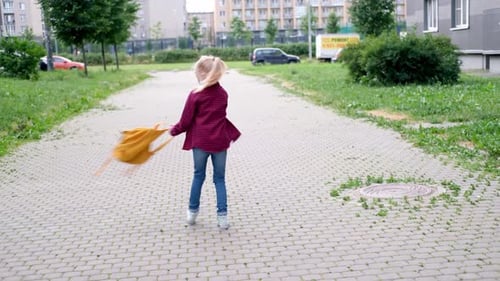Blonde Girl Playing on Street Spinning with Backpacks After School