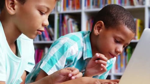 Schoolkids using laptop in library at school