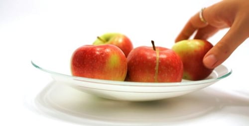 Hand Removing Apples from Plate on White Background