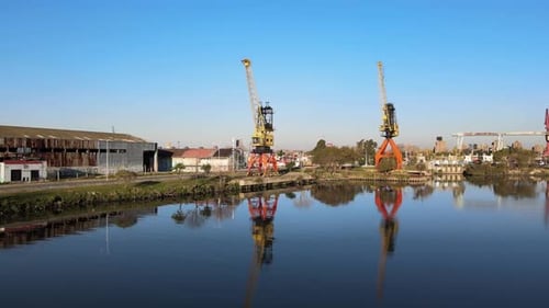 4K Drohnenaufnahmen von zwei großen Kranen entlang der Wasserkante mit klaren Reflexionen neben einem Wa