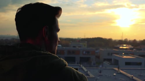 Ein Mann, mit dem Hinterkopf zur Kamera, schaut sich bei Sonnenuntergang in der Stadt unter ihm um