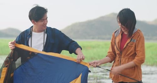 Couple Camping by Lake Setting Up Tent Together