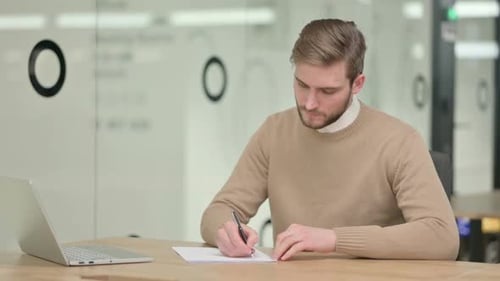 Creative Young Man Writing on Paper in Office