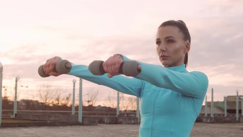 Woman Exercises Shoulders with Weights at Sunset