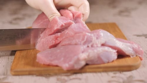 Gloved Hands Carefully Slicing Raw Meat on Board