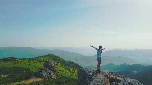 Woman Stands Atop Mountain Peak With Arms Outstretched
