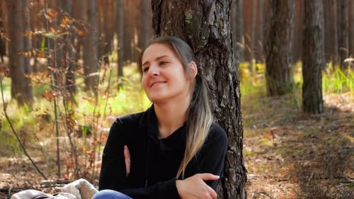 Video einer schönen lächelnden Frau, die sich entspannt, während sie auf dem Boden im Wald oder Park sitzt und sich lehnt