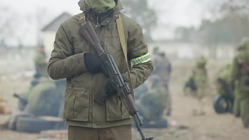 Nicht wiederzuerkennender männlicher Soldat, der mit bewaffneter Gewehrwaffe im Freien steht, als verschwommene Rekruten