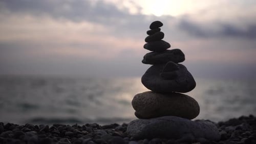 Balanced Pebbles Pyramid on the Beach on Cloudy Day and Clear Sky at Sunset