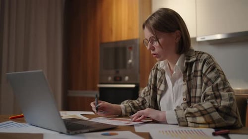 Portrait of a Woman with Glasses Working Remotely in a Home Office at a Desk with a Laptop and Notes