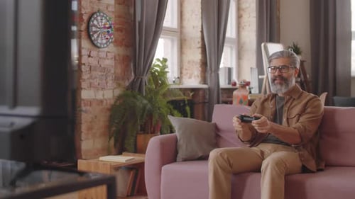 Mature Man Enjoys Video Games on Couch Indoors