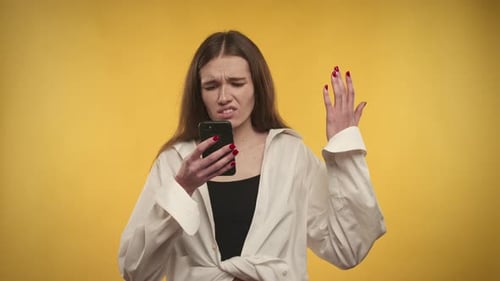 Woman Frustrated with Phone against Yellow Background