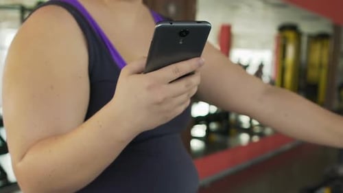 Overweight Girl Taking Break to Regain Breath and Check Mail on Smartphone, Gym