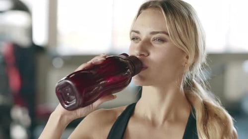 Thirsty Woman Enjoying Water After Fitness Training in Gym