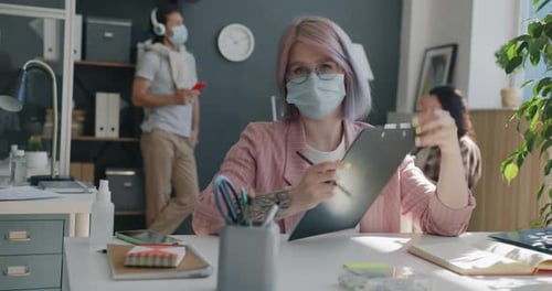 Portrait of Young Woman Making Video Call From Office Wearing Mask Looking at Camera and Speaking
