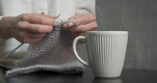 Hands Knitting Gray Wool Next to Coffee Cup
