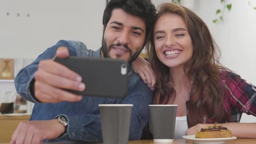 Happy couple with phone making video call in cafe