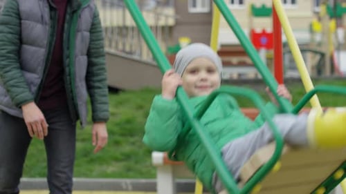 Glücklicher kaukasischer Junge reitet auf Schaukel und Papa schiebt