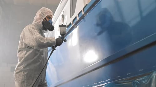 Worker Sprays Blue Paint on Vehicle in Garage