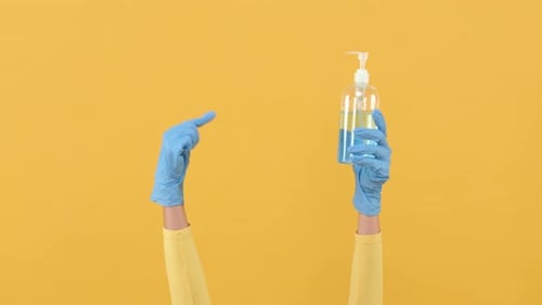Hand Wearing Glove Holding Bottle of Hand Sanitizer