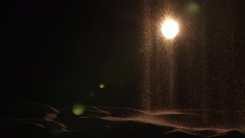 Particles of Dry Sand are Pouring Down on Black Studio Background with Backlight